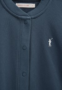 Mørkeblå cardigan med knapper, med ribstrikket krave og knapstolpe, prydet med en lille hvid polo-spillerlogo på venstre bryst og Polo Club-mærke indvendigt.