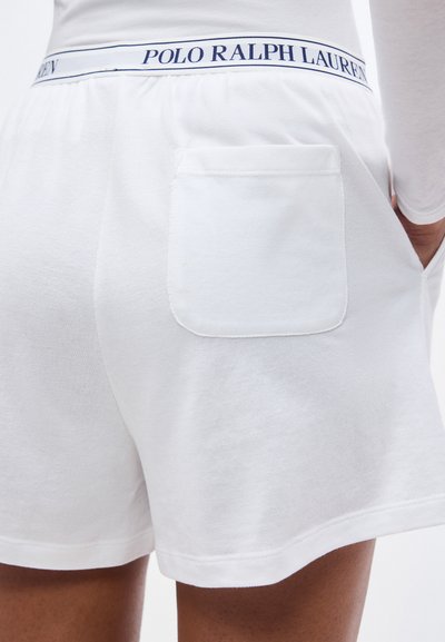 Λευκά πλεκτά σορτς με πίσω τσέπη και ζώνη μέσης με το λογότυπο "Polo Ralph Lauren", φορεμένα με λευκή μακρυμάνικη μπλούζα.