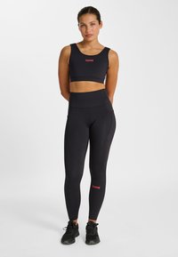 Svart sport-bh och högmidjade leggings av stretchigt material, med en röd logotyp på tyget, designade för aktivt bruk.