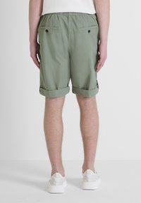 Pantaloni corti verde oliva con orli arrotolati, vita elasticizzata e due tasche posteriori con chiusura a bottone. Tessuto dalla consistenza liscia.
