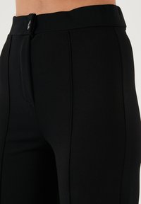 Black tailored trousers with a flat front, slim fit, textured fabric, and a waistband featuring a button closure.