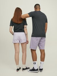 Dos personas están de espaldas, vistiendo camisetas negras. La mujer lleva pantalones cortos de color púrpura claro, mientras que el hombre también lleva pantalones cortos de color púrpura claro y zapatillas negras.