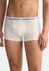 Boxeri din bumbac alb cu un design ajustat, având o bandă logo bleu în talie și picioare scurte, prezentate pe o siluetă masculină.