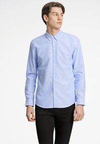Camicia azzurro chiaro con colletto a punta, maniche lunghe e orlo arrotondato. Realizzata in un tessuto liscio e leggermente strutturato.
