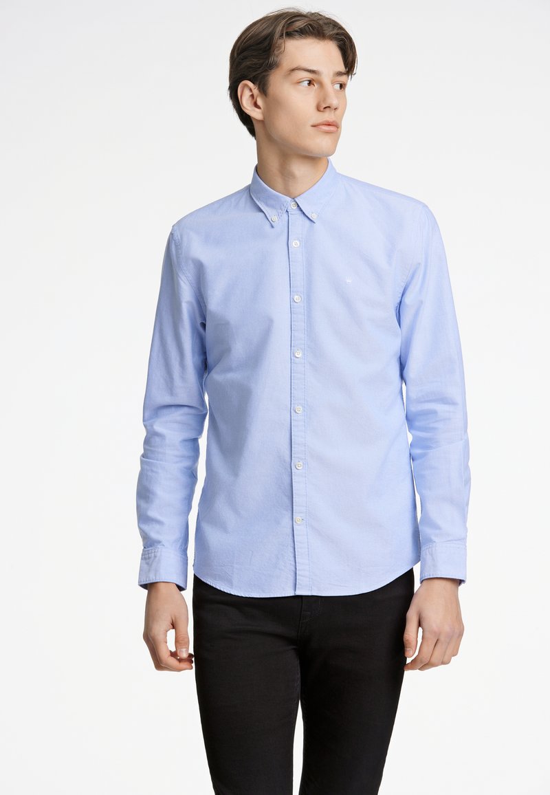 Camicia azzurro chiaro con colletto a punta, maniche lunghe e orlo arrotondato. Realizzata in un tessuto liscio e leggermente strutturato.