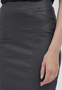 Jupe crayon en cuir gris foncé avec des coutures visibles et des détails de coutures angulaires. Présente une texture lisse et une silhouette ajustée.