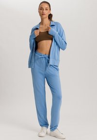 Svetle modrá sportovní souprava obsahující zipovou bundu a kalhoty na šňůrku. Na vrchní části je hnědý crop top. Měkká, hladká látka s uvolněným střihem.