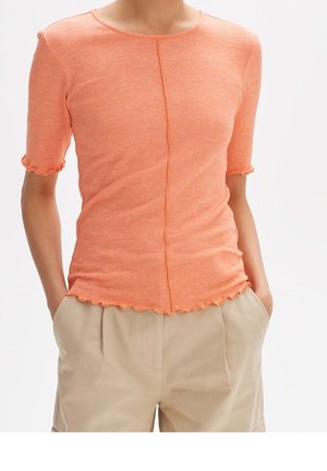 Krótkim rękawem, koralowo-pomarańczowa bluzka z okrągłym dekoltem, teksturowaną tkaniną i falowanymi krawędziami wzdłuż rękawów i dołu.