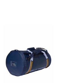 Sac de sport cylindrique bleu marine avec des accents blancs et dorés, fabriqué en tissu durable, doté de sangles latérales et d'une poche pour étiquette.