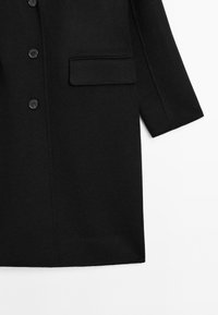 Czarny wełniany płaszcz o prostym kroju, z dużymi guzikami, pojedynczą kieszenią na piersi i otwartym fasonem rękawów. Gładka textura.