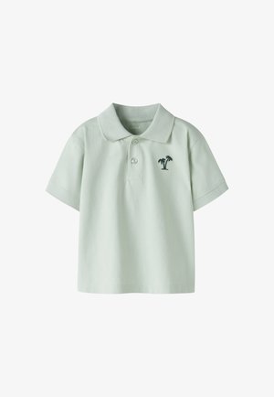 Hellgrünes Poloshirt mit kurzen Ärmeln, Kragen, zwei Knöpfen und kleinem dunkelgrünen Palmen-Stick auf der linken Brust.