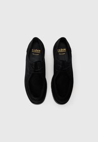 Chaussures en daim noir avec un bout rond, peu de coutures et une semelle en caoutchouc texturée. Comprend des lacets et un logo de marque en relief sur la semelle intérieure.