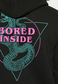 Felpa nera con grafica di un serpente neon blu avvolto attorno al testo rosa "BORED INSIDE" su un contorno a forma di triangolo sul retro.