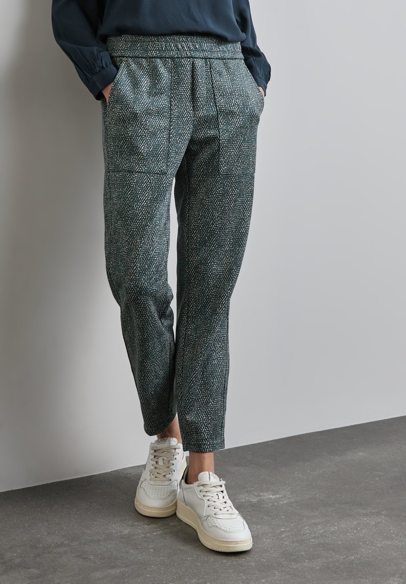 Gestructureerde groene houndstooth broek met een taps toelopende snit, voorzien van plooien aan de voorkant en zijzakken, gecombineerd met witte sneakers.
