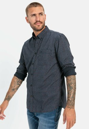 Donkerblauwe button-up shirt met een geometrisch patroon in rood en wit, lange mouwen opgerold bij de manchetten, voorzien van een enkele borstzak.