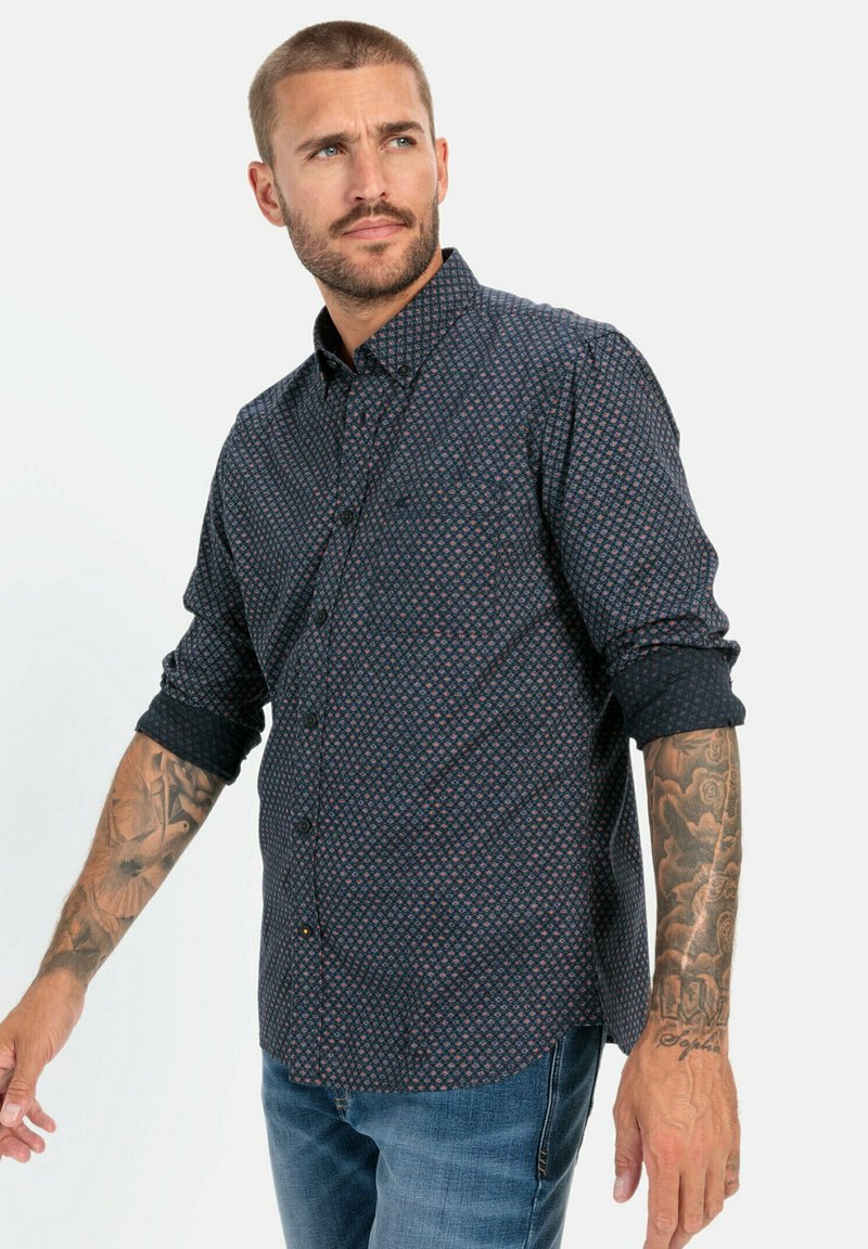 Donkerblauwe button-up shirt met een geometrisch patroon in rood en wit, lange mouwen opgerold bij de manchetten, voorzien van een enkele borstzak.