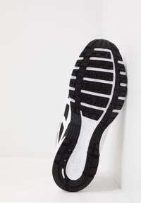 Černobílá podrážka sportovní obuvi s texturovanou gumou pro lepší grip, která obsahuje drážkovaný vzor a akcent střední části. Design zahrnuje zakřivené okraje.