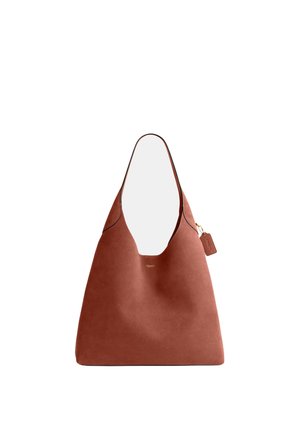 Sac cabas en cuir marron avec une large bandoulière unique, petit logo Coach doré et étiquette en cuir attachée sur fond blanc.