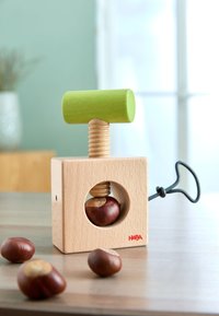 Wooden chestnut press with a green handle, light wooden body, and a circular hole revealing a chestnut. Features a black metal screw mechanism.