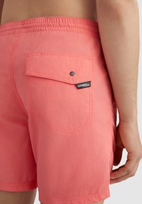 Shorts de bain rose clair en tissu léger, dotés d'une taille élastique, d'une poche latérale et d'une étiquette de marque sur la poche arrière.