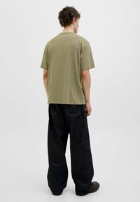 Oliven grøn bomulds t-shirt med en afslappet pasform, parret med mørkeblå, brede bukser med synlige sømme og baglommer.
