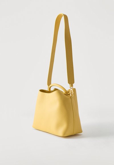 Κίτρινη δερμάτινη τσάντα με υφή στην επιφάνεια, φαρδιά ρυθμιζόμενη λουρά ώμου και μικρότερη καμπυλωτή λαβή στην κορυφή.