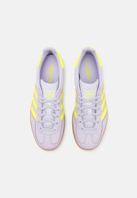 Světle fialové sportovní boty se žlutými pruhy, hladký kožený svršek, polstrovaný límec a gumová podrážka. Obsahují splétané tkaničky a akcenty s logem.