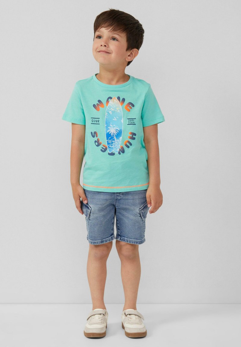 Turquoise t-shirt met korte mouwen met een surfboard-graphic en tekst, gecombineerd met blauwe spijkerbroekshorts en beige schoenen met klittenband.