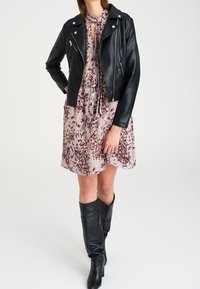 Černá kožená motorkářská bunda přes šaty s květinovým potiskem v pastelových odstínech. Černé kožené boty po kolena. Hladké textury a padnoucí střih.