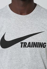 Camiseta gris de manga corta hecha de una mezcla de algodón, con un gran logo en negro de Nike y el texto "TRAINING" en letras negritas negras.