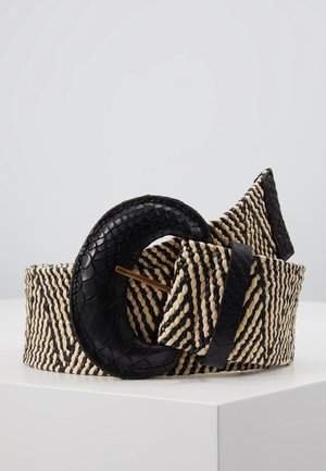 Ceinture tissée noire et beige avec une grande boucle circulaire noire texturée, présentée enroulée sur une surface blanche.