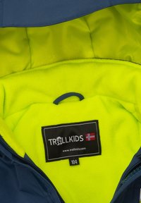 Tela exterior azul con forro de felpa amarilla brillante. Presenta una etiqueta con "TROLLKIDS" y tamaño "104". Textura suave, diseño funcional.