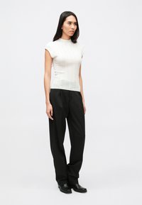 Εφαρμοστή λευκή πλεκτή μπλούζα με κοντά μανίκια, υφή υφάσματος, συνδυασμένη με ψηλόμεσα μαύρα παντελόνια και μαύρα μποτάκια μέχρι τον αστράγαλο.