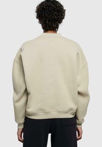 Beige oversized genser med senkede skuldre, ribbestrikkede mansjetter og nederkant. Glatt tekstur med minimale sømdetaljer bak.