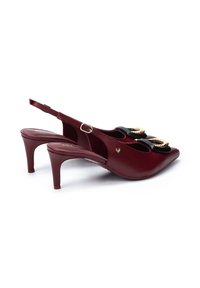 Tacones de charol burdeos con tiras laterales, punteras afiladas y detalles en metal dorado. Tacones delgados de aproximadamente 7.5 centímetros de altura.