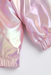Manches de veste élastiquées roses iridescentes et brillantes avec des poignets froncés, mettant en avant une texture de tissu lisse et réfléchissante.