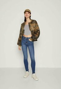 Kareivinis bomberis, per didelis, pilkas trumpas švarkas, mėlyni siauri džinsai ir smėliniai sportbačiai. Priedai – smėlio spalvos kepurė.