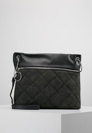 Sac bandoulière matelassé noir avec dessus en cuir rabattable, fermeture éclair argentée, porte-clés et sangle amovible sur une surface blanche.