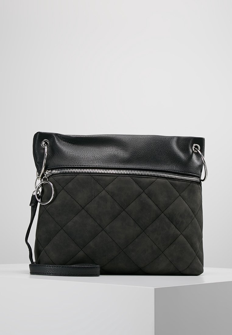 Sac bandoulière matelassé noir avec dessus en cuir rabattable, fermeture éclair argentée, porte-clés et sangle amovible sur une surface blanche.