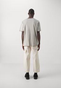 Jasnoszara koszulka z krótkim rękawem o luźnym kroju, w połączeniu z off-white dżinsami, które mają detale kieszeni bocznych oraz taperowany krój nogawki.
