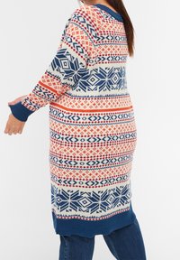 Lång stickad tröja med ett flerfärgat geometriskt mönster i röd, blå och krämfärgad. Designen sträcker sig till muddar och fåll i blått.