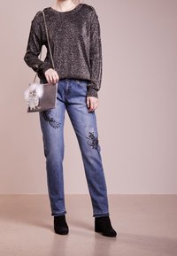 Maglione in maglia nera con glitter e maniche lunghe, abbinato a jeans in denim blu con ricami di uccelli. Stivaletti neri e borsa a forma di gufo.