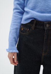 Light blue, ribbed knit sweater with frayed cuffs paired with dark denim jeans featuring orange stitching and a front pocket.