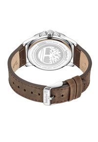Correa de reloj de cuero marrón con caja de acero inoxidable plateada, con un fondo redondo grabado con el logo. Resistente al agua hasta 3 ATM.