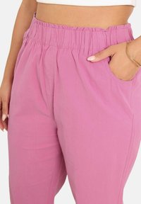 Vaaleanpunaiset rentoistuvat housut, joissa on joustava vyötärö ja sivutaskut. Ne on valmistettu kevyestä kankaasta, joka tarjoaa sileän pinnan.