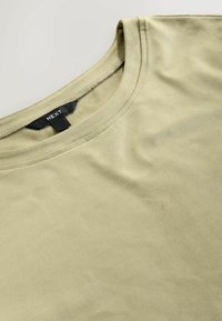Olivengrøn T-shirt med korte ærmer lavet af blødt stof, rund hals og minimale syninger. Mærket viser "NEXT."