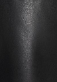 Surface en cuir noir texturé avec un motif de grain subtil et un doux reflet de lumière verticale au centre.