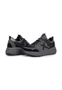 Chaussures de sport grises mettant en avant une combinaison de matériaux lisses et texturés, des accents noirs et une semelle grise mouchetée. Des détails réfléchissants améliorent la visibilité.