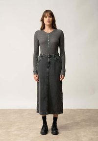 Szara, prążkowana bluzka z długim rękawem i zapięciem na guziki, zestawiona z ciemnoniebieską spódnicą midi z dżinsu. Czarne buty na platformie dopełniają stylizację.