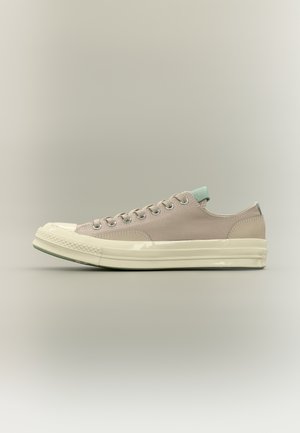 Beiger Sneaker mit niedrigem Schaft, cremefarbener Gummisohle und Zehenschutzkappe, hellgrünem Fersenlasche und Zungenetikett, sichtbaren Metallösen und Obermaterial aus Textil.